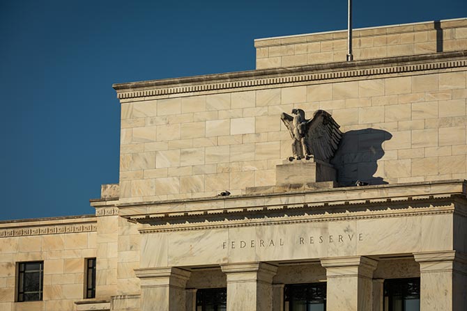 Staying Power; Exterior of the Federal Reserve building with a stone eagle sculpture. The architecture is classical with beige stone under a clear blue sky.