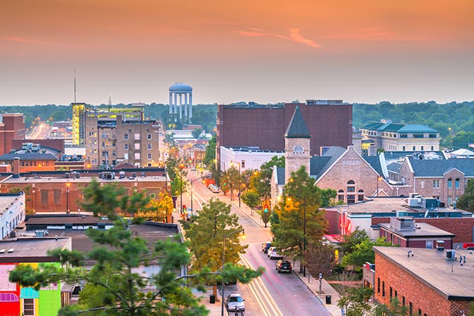 Community Banking Month; A scenic view of a city at sunset, with vibrant orange skies. Buildings and a church line the bustling street. A distant water tower is visible on the horizon.
